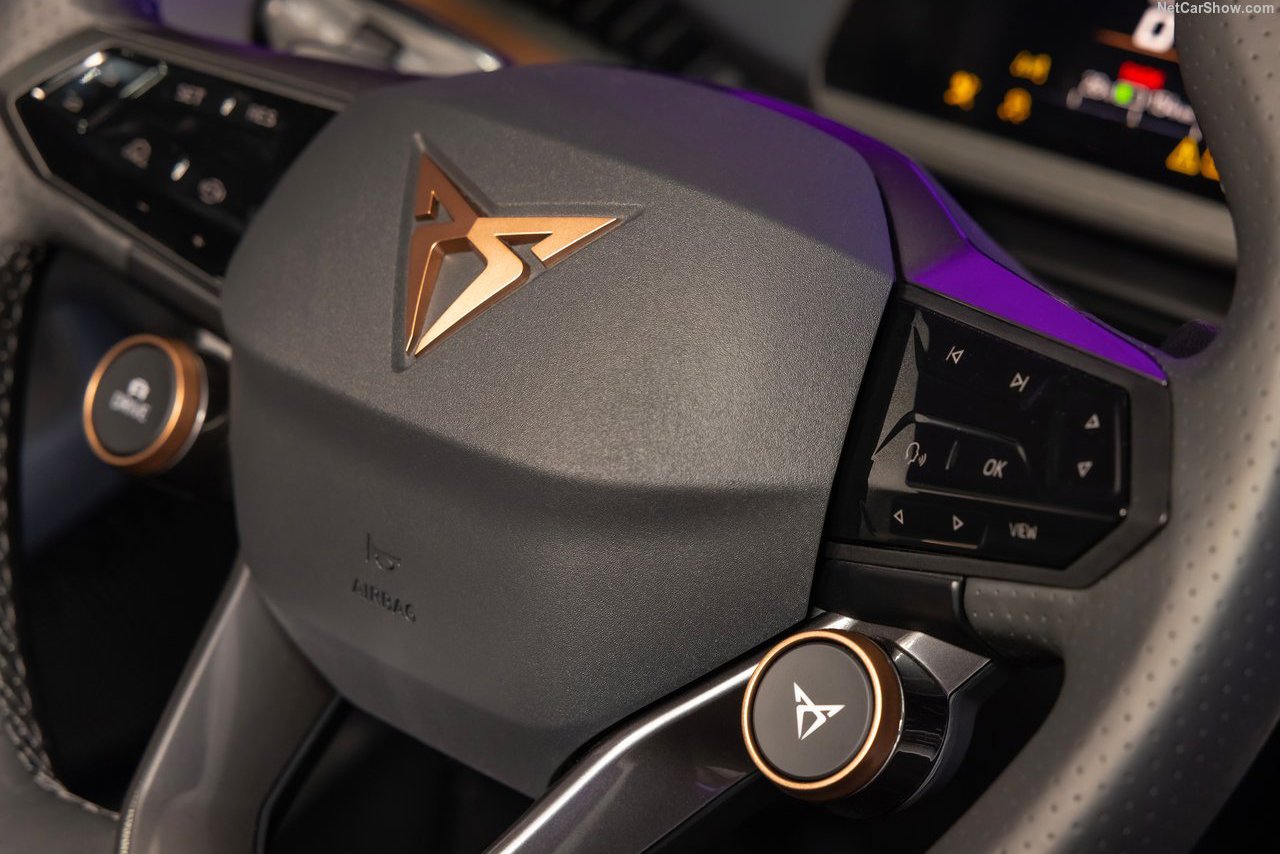 A detailed view of the Cupra Tavascan's steering wheel, featuring the brand’s logo, integrated controls, and premium finishes with bronze accents.