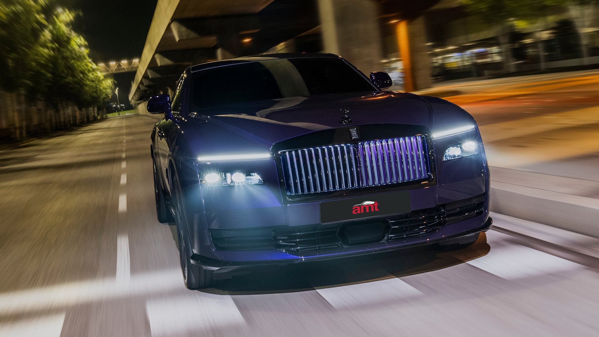 Front view of the Rolls-Royce Spectre Black Badge driving at night, with its illuminated grille and striking LED headlights creating an imposing road presence.