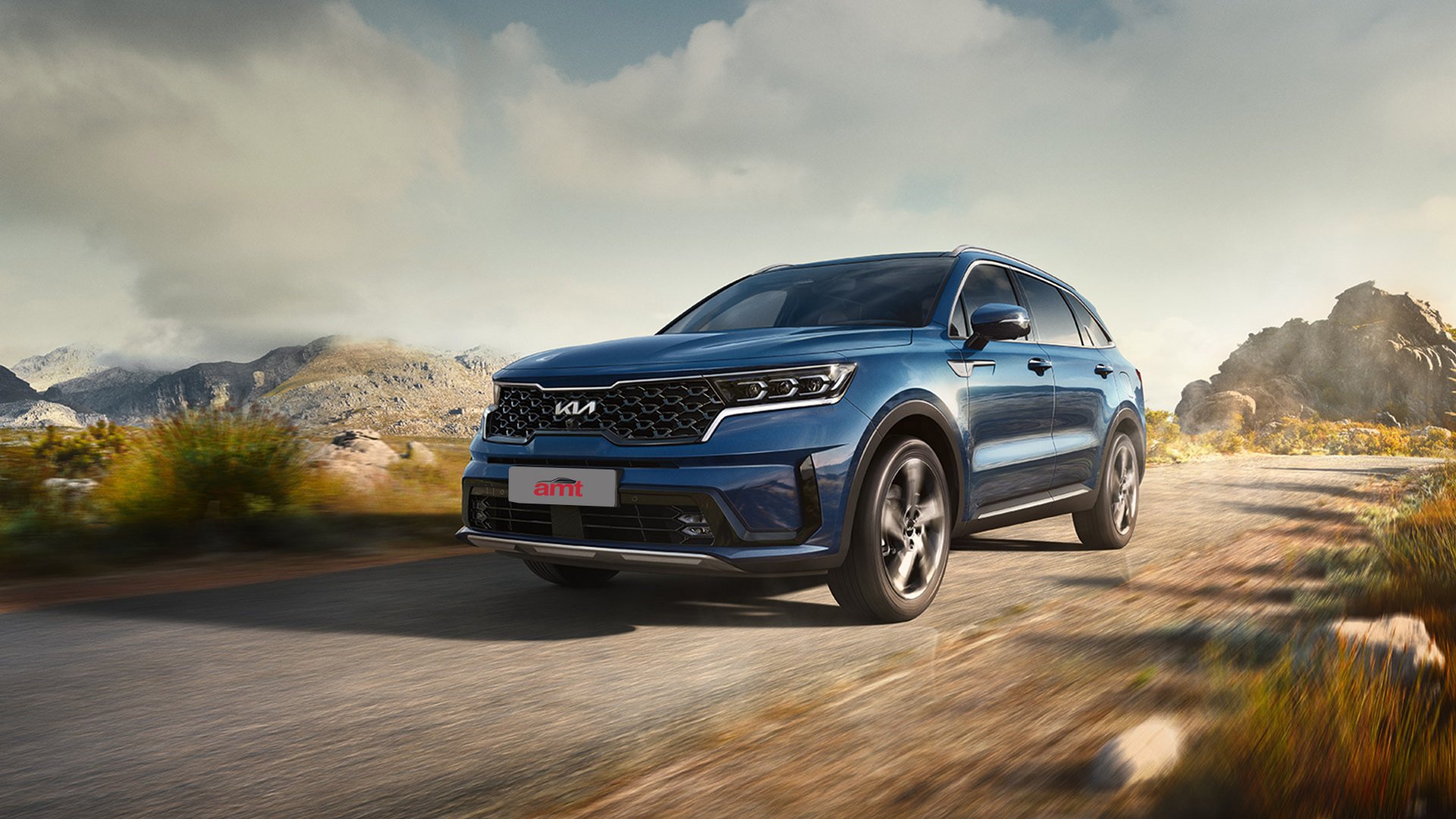 A blue Kia Sorento, a modern and spacious 7 seater car, driving on a scenic countryside road with rugged mountains and a clear sky in the background.