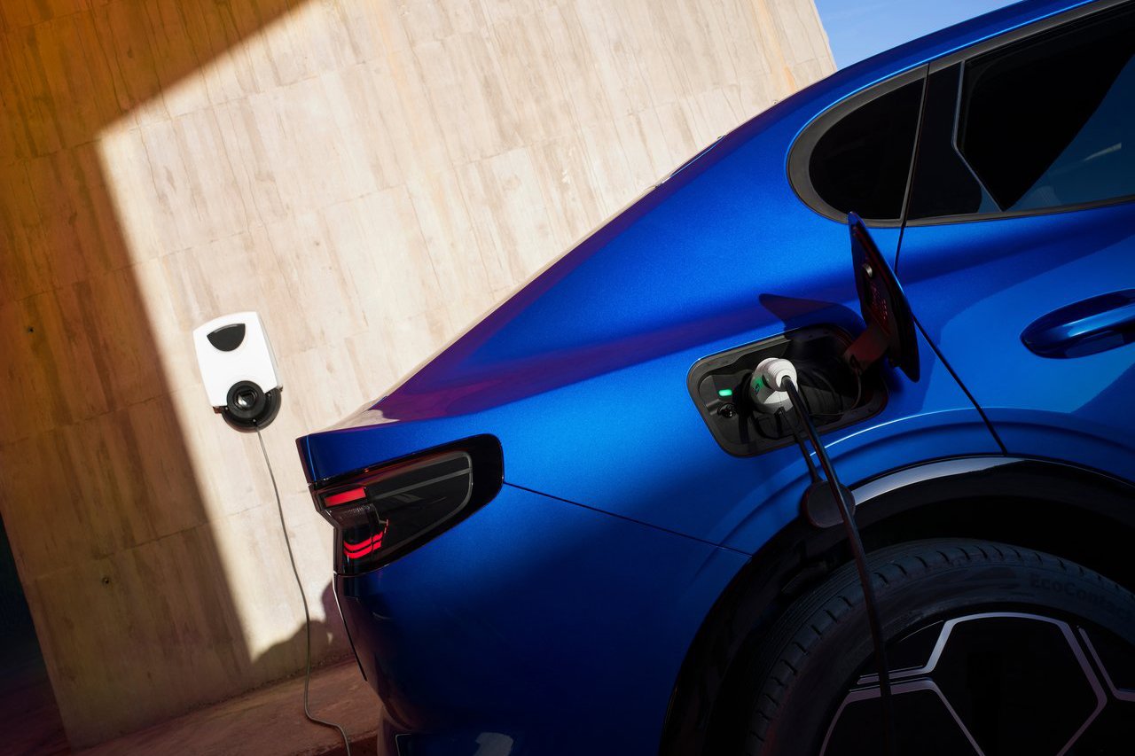 The rear quarter view of a blue Ford Capri plugged into a home charging station, highlighting its electric capabilities and modern lifestyle compatibility.