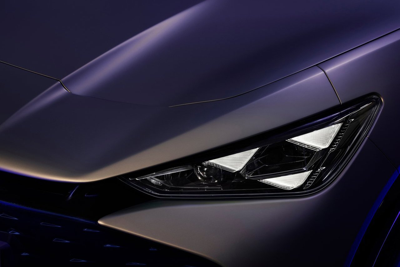 [A close-up of the Cupra Tavascan's angular headlight, emphasising its sharp and dynamic design illuminated under soft purple lighting