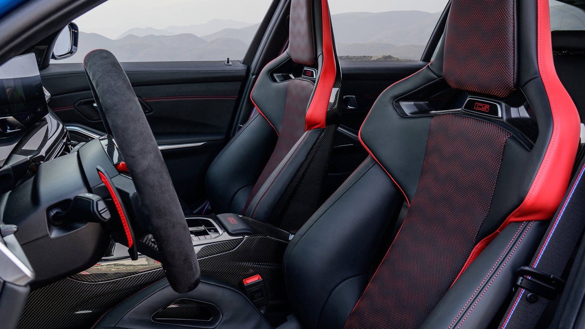 A close-up of the BMW M3 CS Touring interior, featuring M Carbon bucket seats with red accents, Alcantara-wrapped steering wheel, and carbon fibre details.