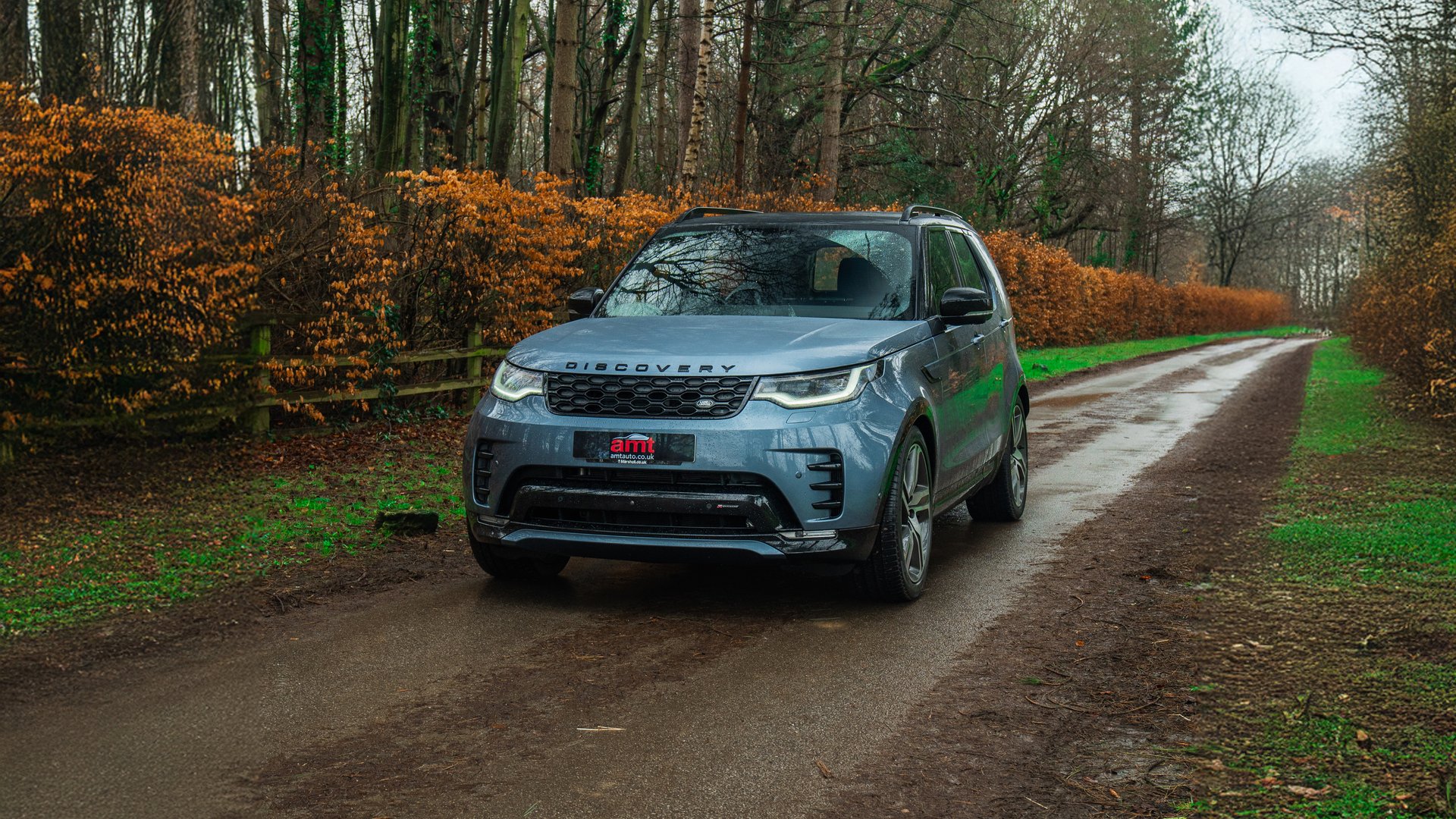 A grey Land Rover Discovery, a versatile 7 seater car, parked on a wet countryside road surrounded by autumnal trees and hedges