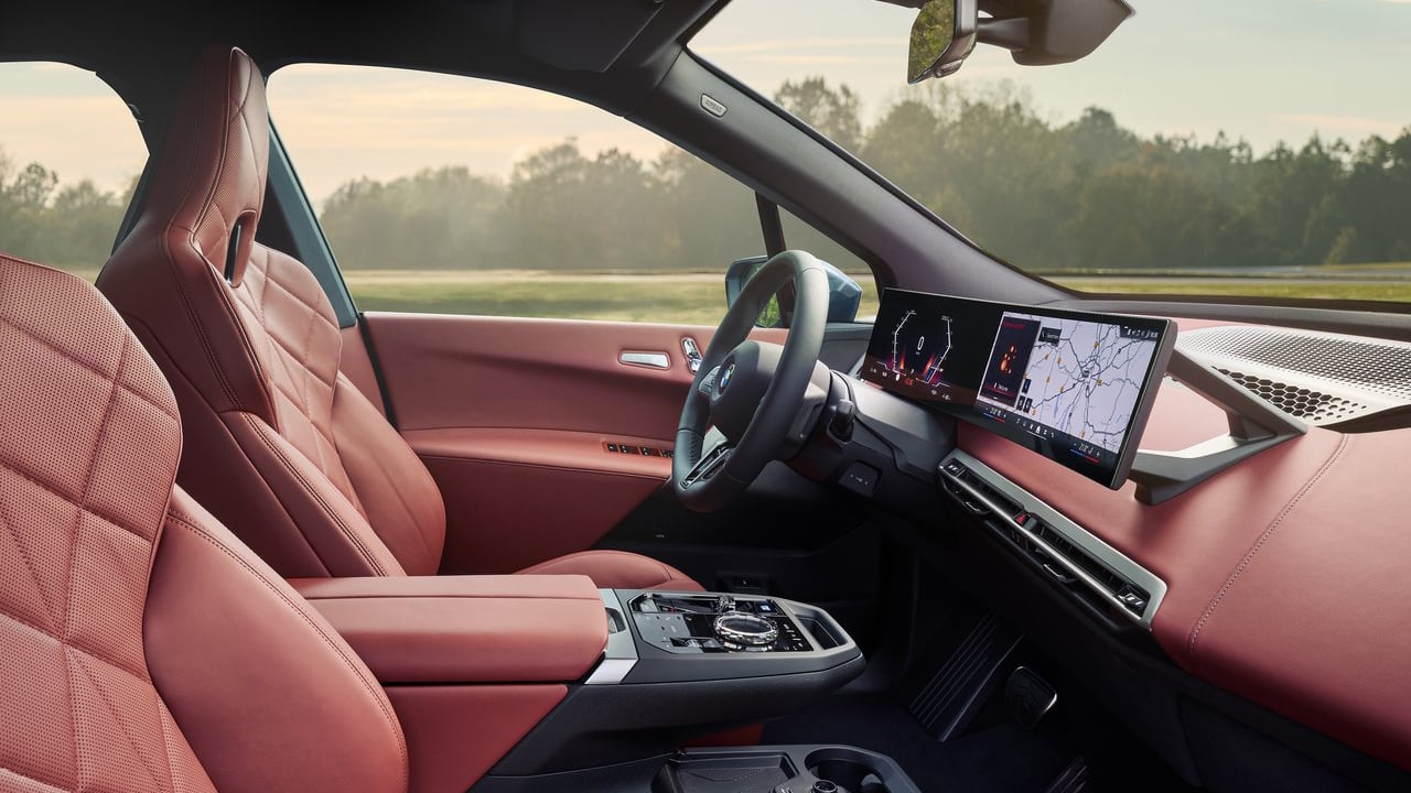 Side view of the interior of the 2025 BMW iX, highlighting the spacious cabin and premium finishes with a large digital display.