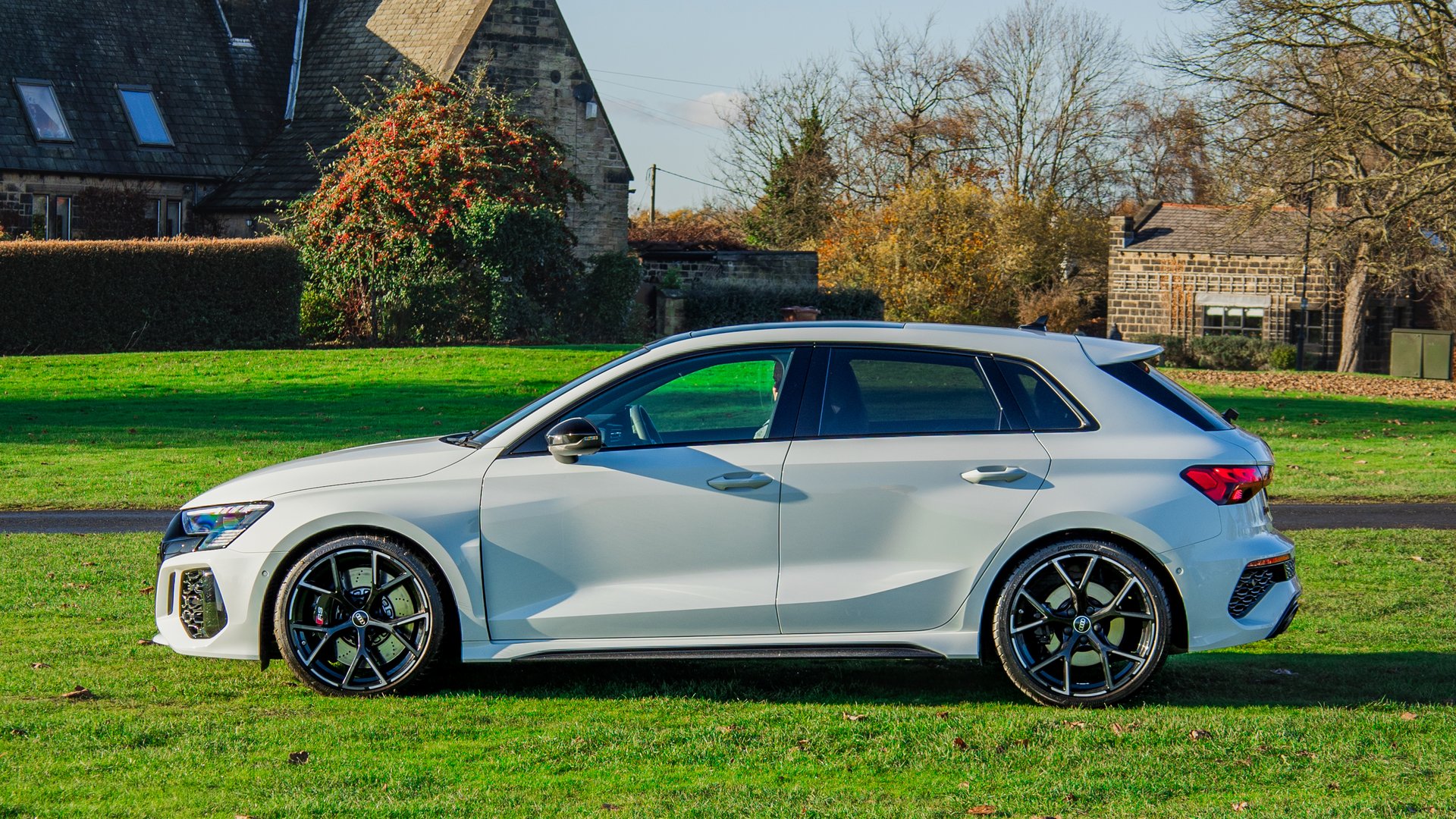 A side profile of the Audi RS3 parked on a lush green lawn, displaying its dynamic silhouette, large alloy wheels, and sporty side accents.