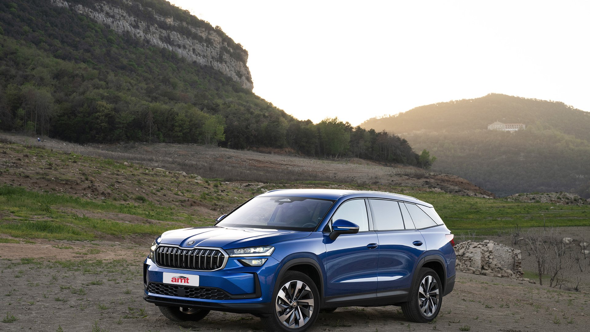 A vibrant blue Skoda Kodiaq, a stylish and practical 7 seater car, parked in a rugged outdoor landscape with rolling hills and a serene sunset in the background.
