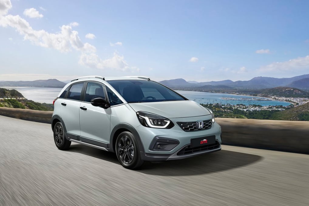 The Honda Jazz in soft grey, zipping through a picturesque coastal road, designed for adventure in 2025.