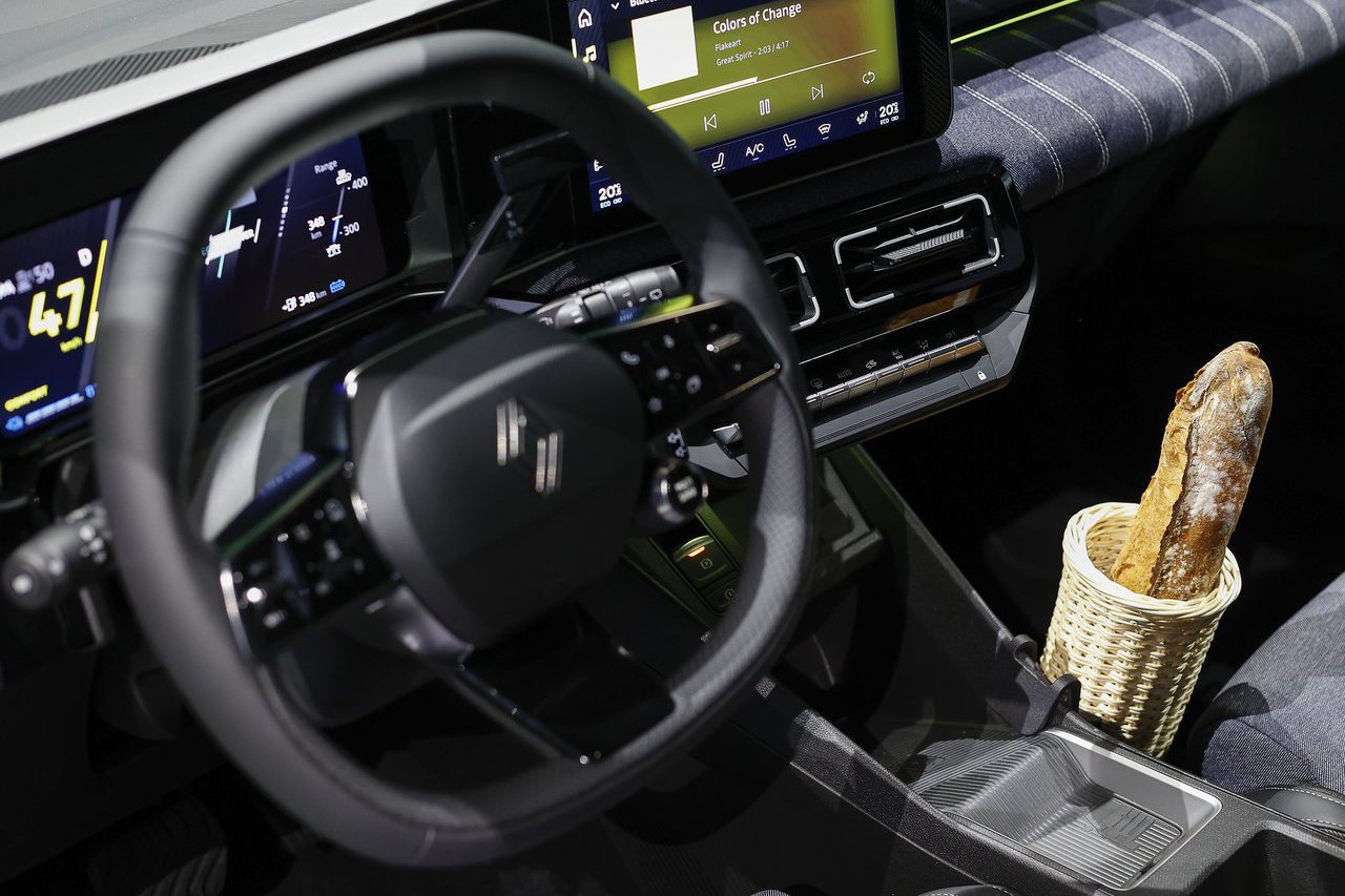 A closer look at the Renault 5’s dashboard featuring a digital screen, infotainment system, and a quirky detail with a baguette placed in the centre console.