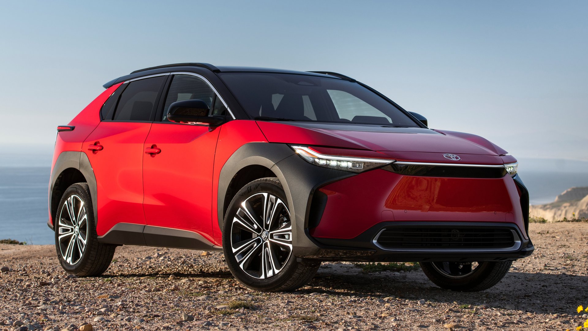 Toyota's fully electric bZ4X in a sleek red and black combination, captured by a serene coastal view for the 2025 release.