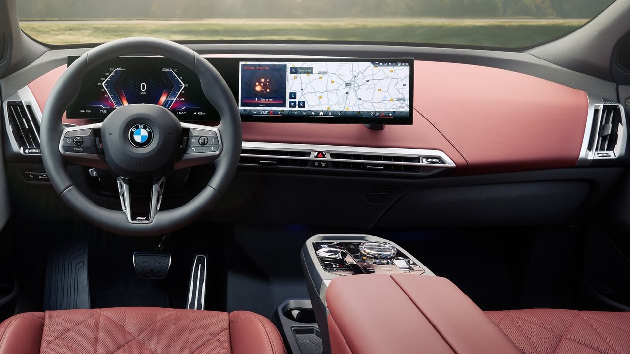 Interior of the 2025 BMW iX showcasing the curved digital display and modern dashboard with a luxurious red leather finish.