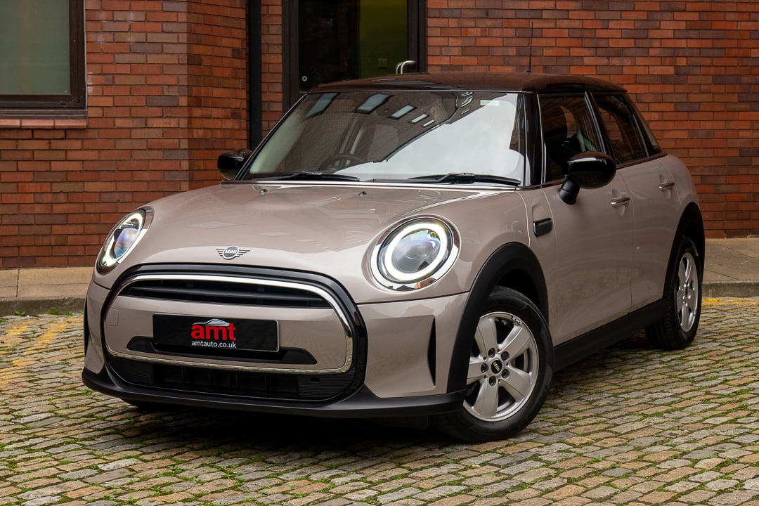 A modern Mini Cooper Electric in beige, parked on a cobblestone driveway, representing compact electric style for 2025.