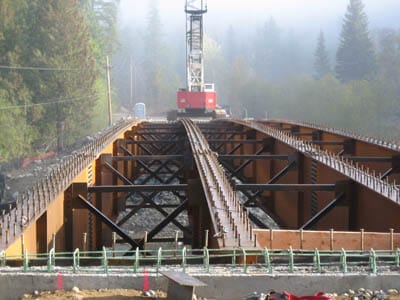 Steel truss bridge under construction at Bear Gulch showing cross-bracing, temporary falsework, and a red vehicle on the deck