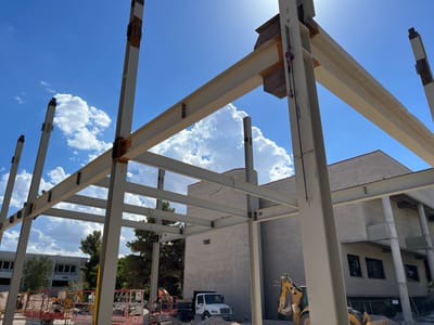Structural steel building frame under construction with white-painted columns and beams against a blue sky with clouds