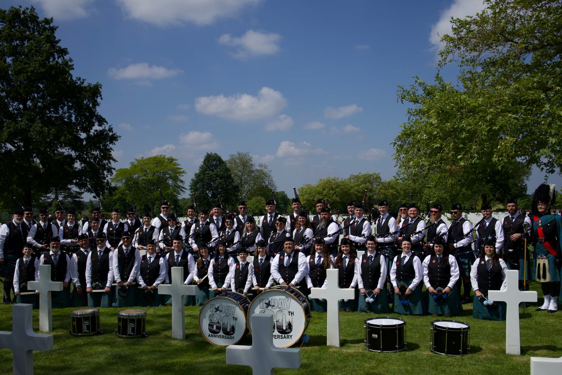 Wide view of the Utah Pipe Band posed among white crosses at an American military cemetery