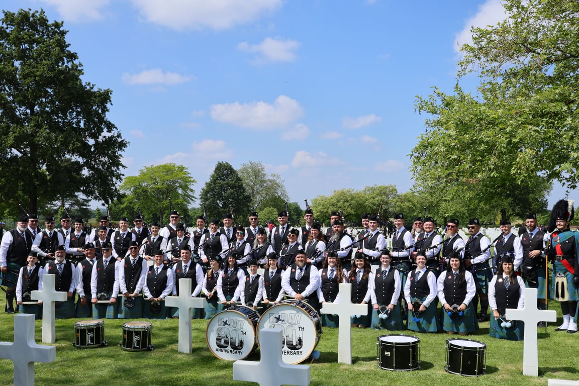 Pipe band in highland dress posed among white crosses at an American military cemetery in Normandy