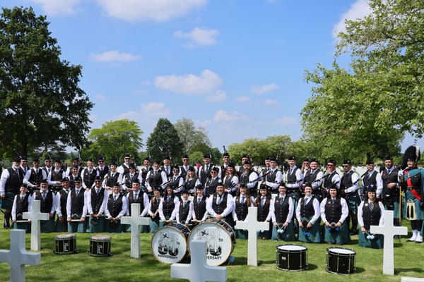 Pipe band in highland dress posed among white crosses at an American military cemetery in Normandy