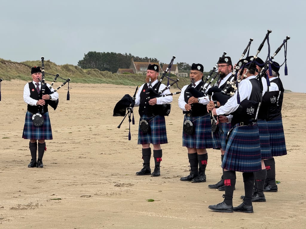 Bagpipers in kilts and highland dress playing on a sandy Normandy beach