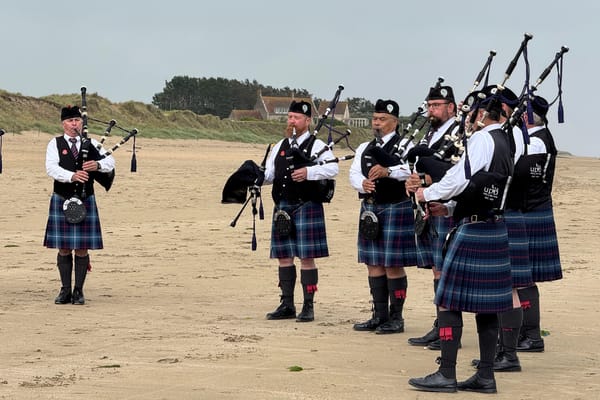 Group of bagpipers in kilts and highland dress playing on a sandy Normandy beach