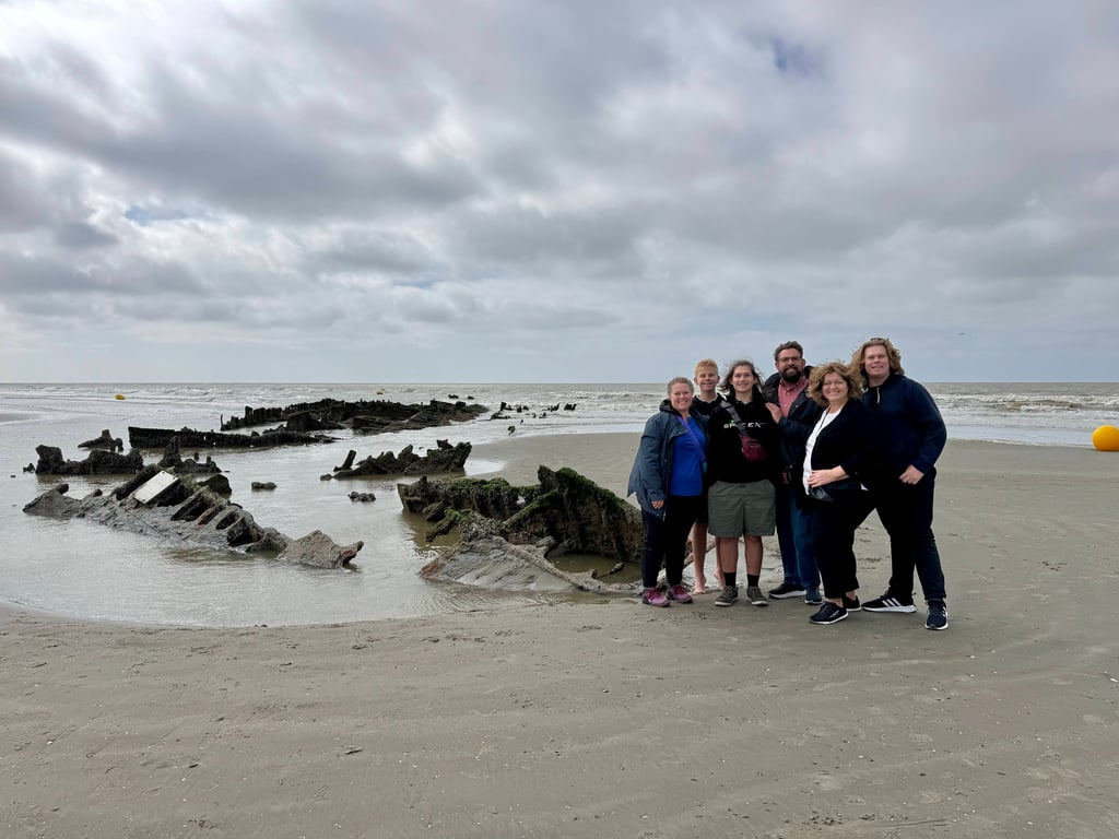Family group on a cloudy beach standing next to rusted WWII wreckage partially buried in sand