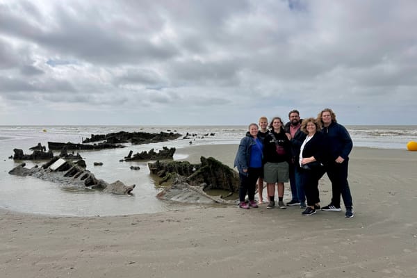 Family group on a cloudy beach standing next to rusted WWII wreckage partially buried in sand