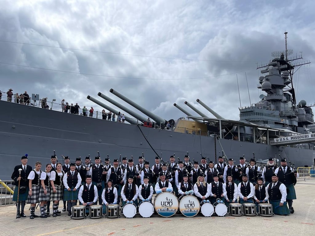 Utah Pipe Band members in full highland dress posed in front of the USS Missouri at Pearl Harbor