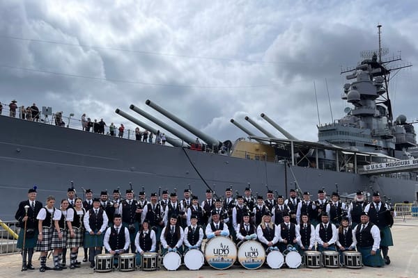 Utah Pipe Band members in full highland dress posed in front of the USS Missouri