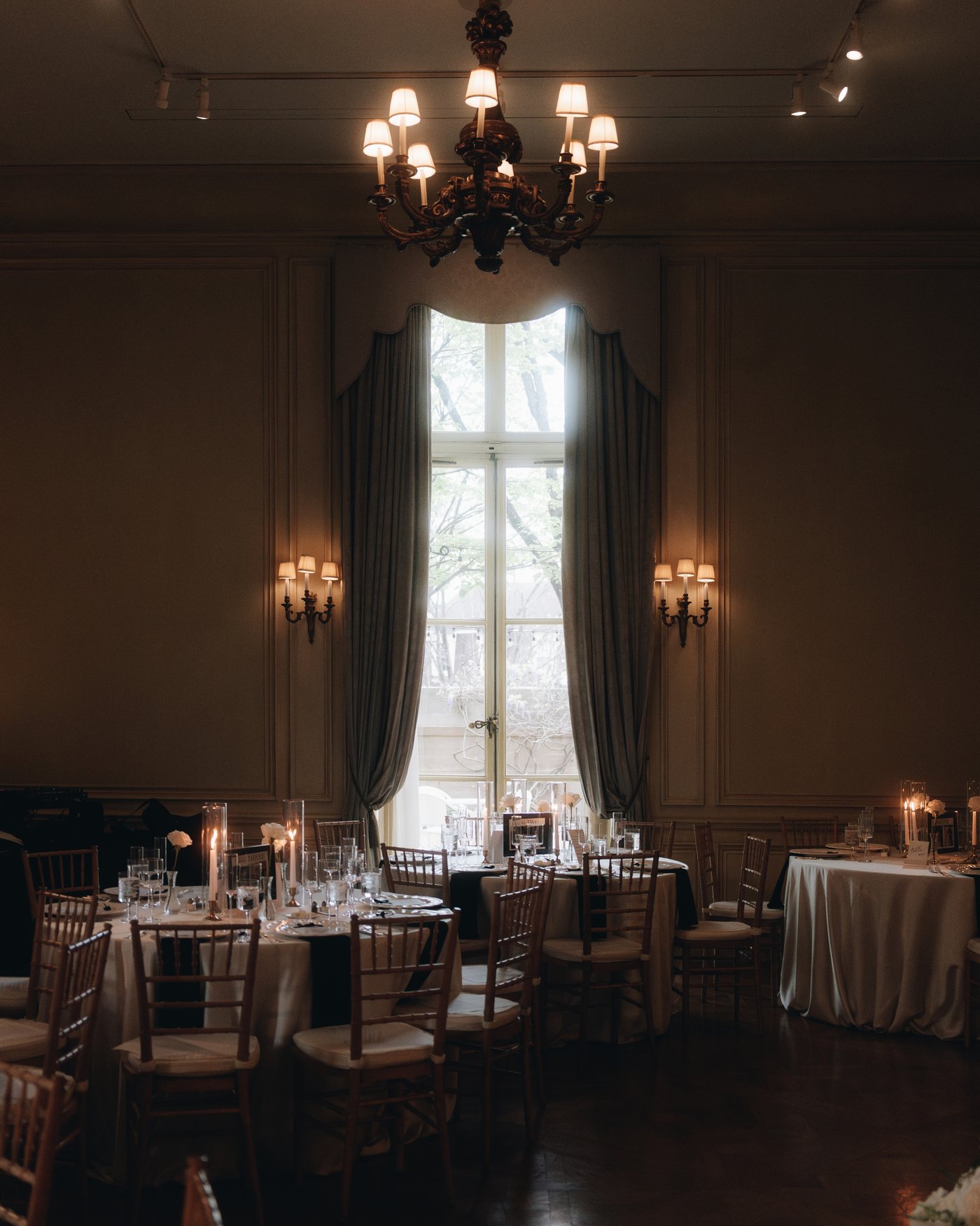 The ballroom set for dinner, round tables and tall curtained windows