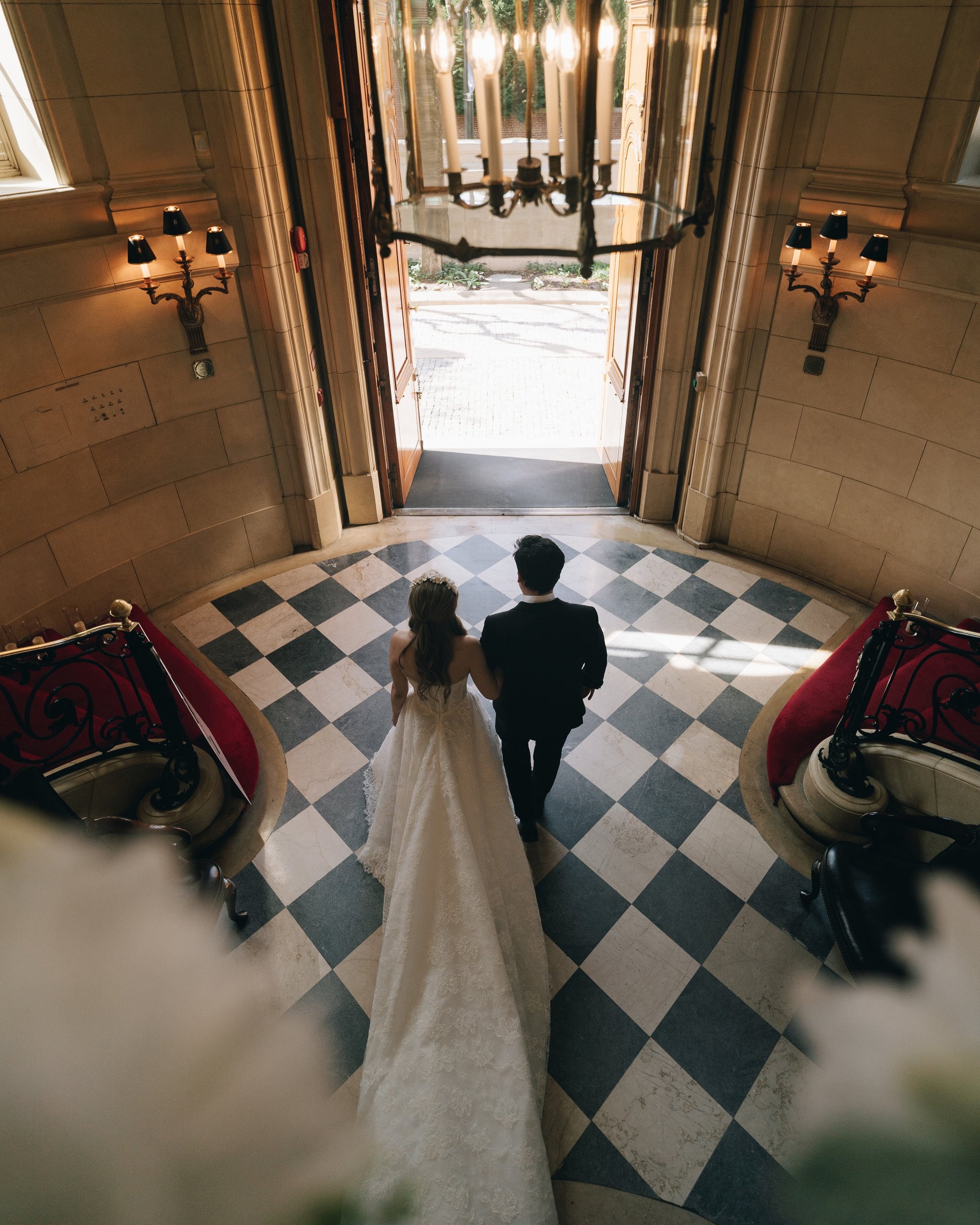 The bride and groom walking away down the black and white marble hall toward the open doors