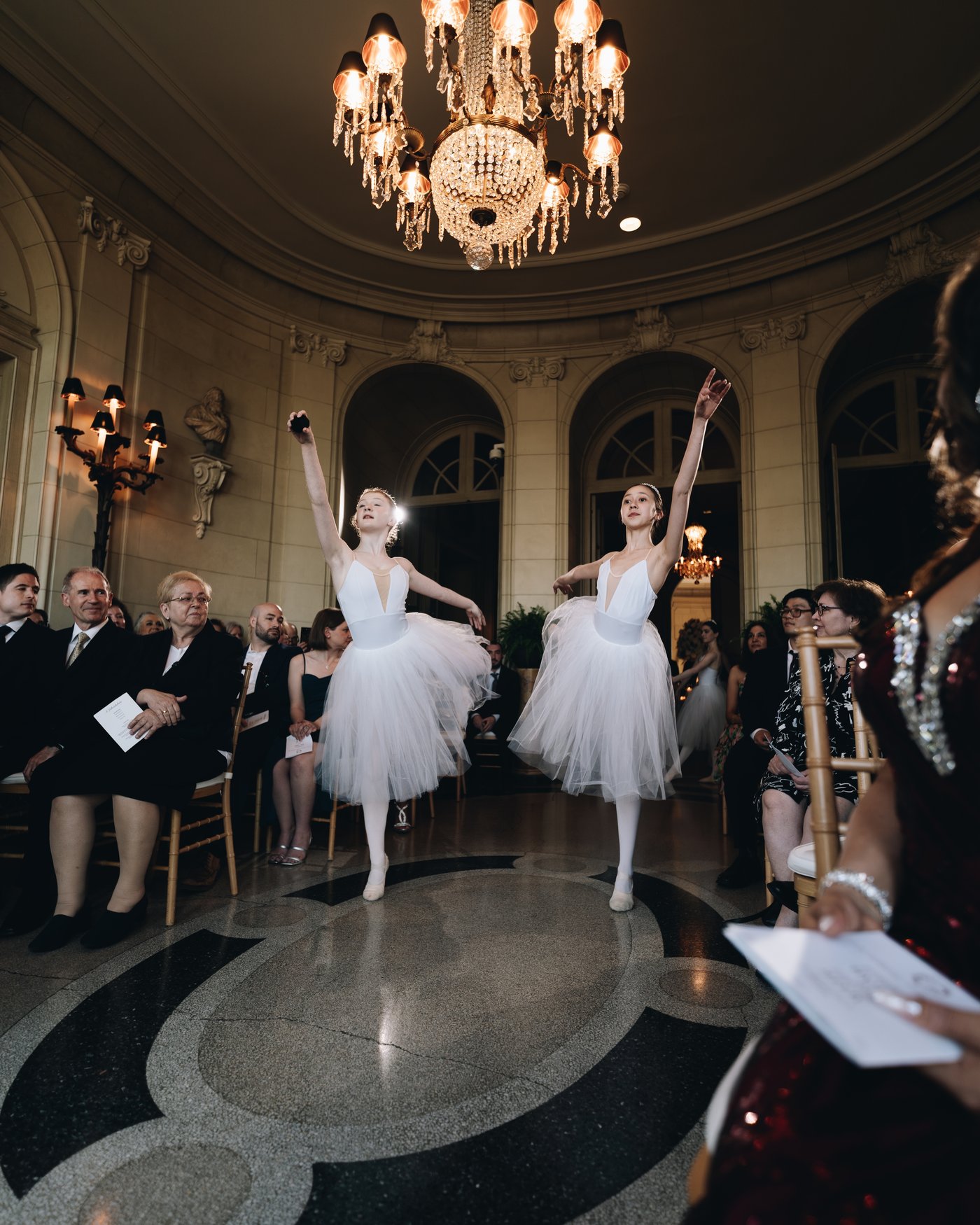 Dancers in white tutus mid performance, the room watching from every side