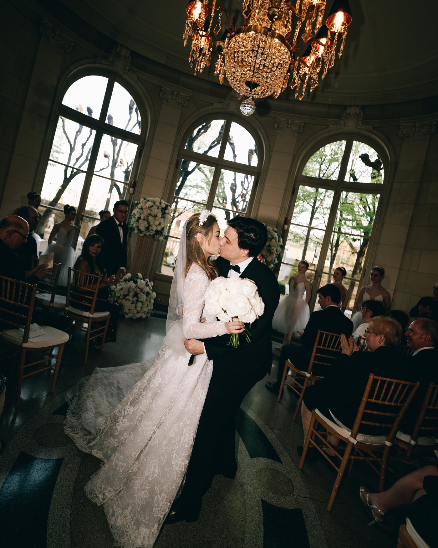 The couple walking through the ballroom beneath the chandeliers