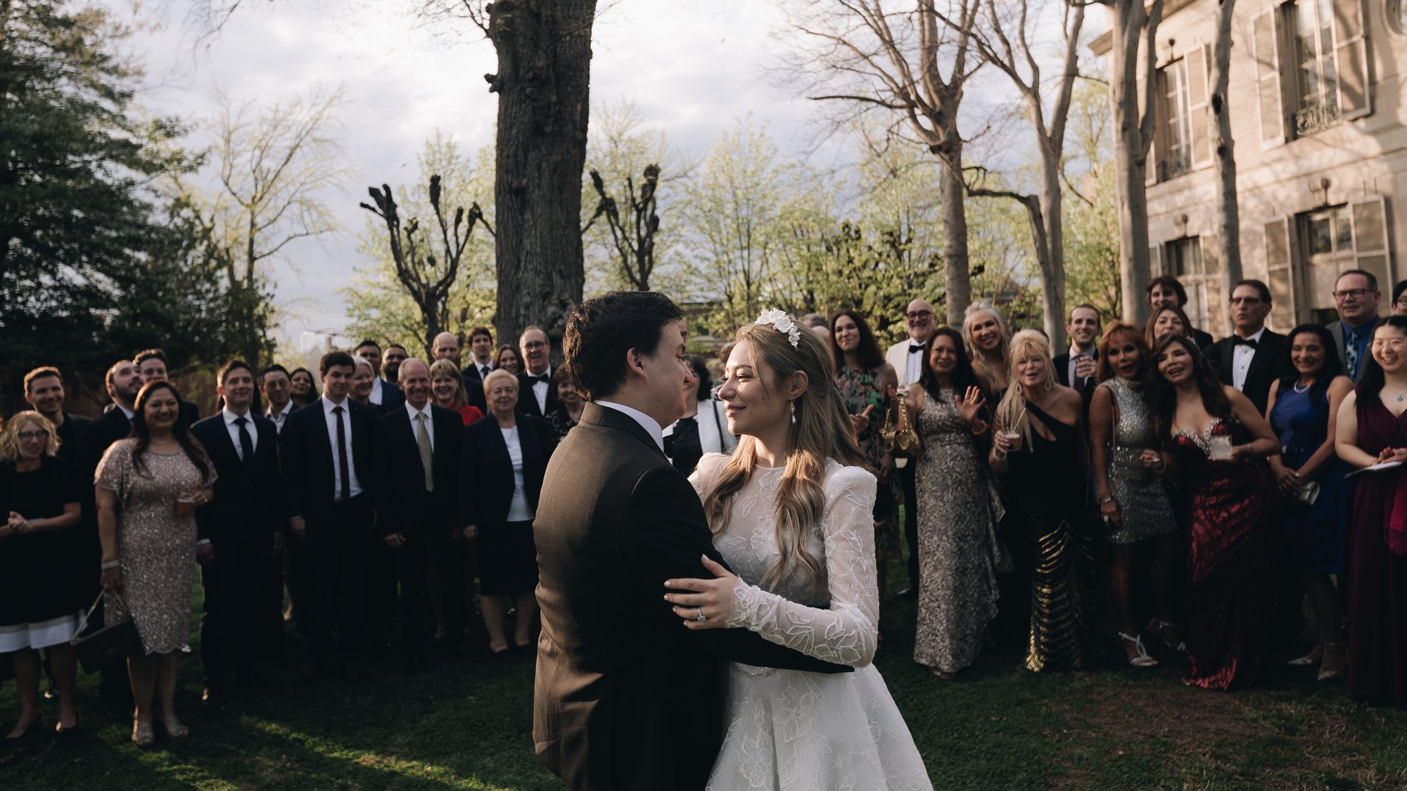 The bride and groom holding each other with the whole party standing around them under the trees