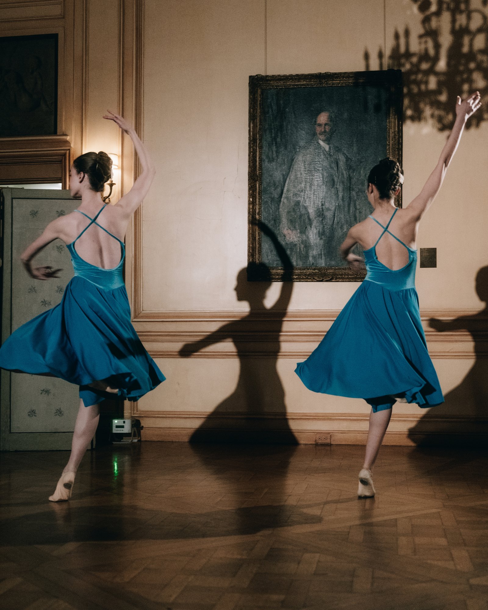 Two dancers in blue, arms raised, under the painting on the ballroom wall after dinner