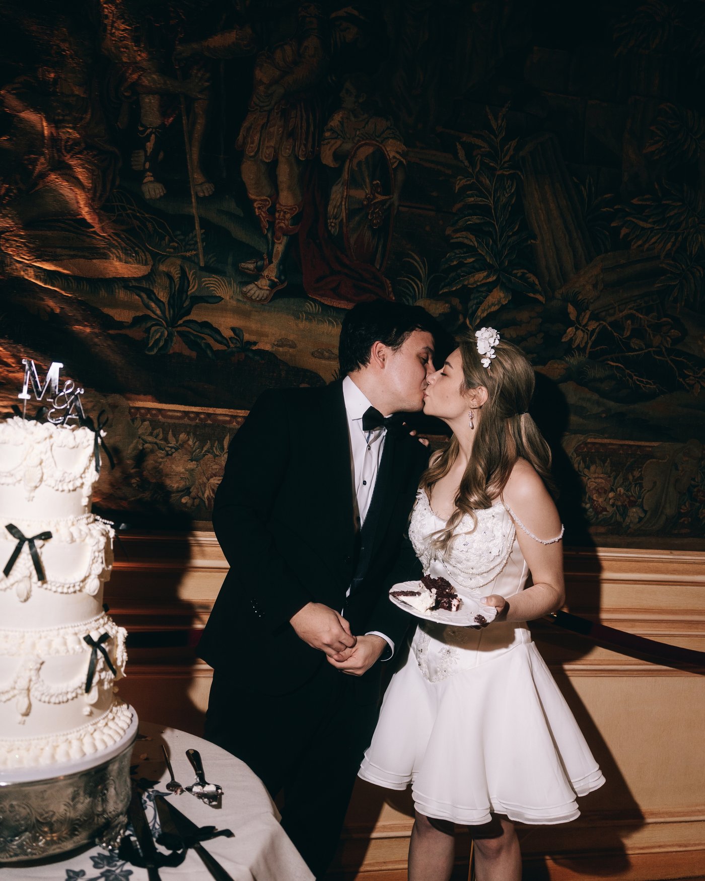 The bride and groom kissing beside the cake, the bride now in a short dress