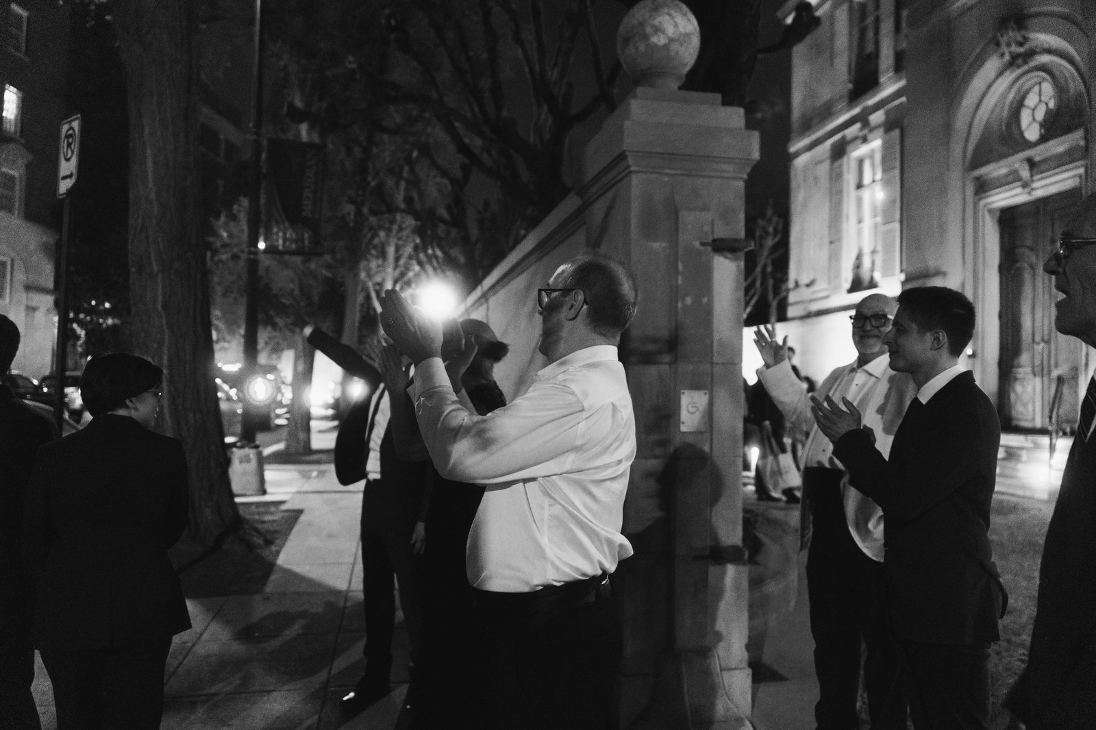 Black and white, the couple holding each other outside at night while the guests look on