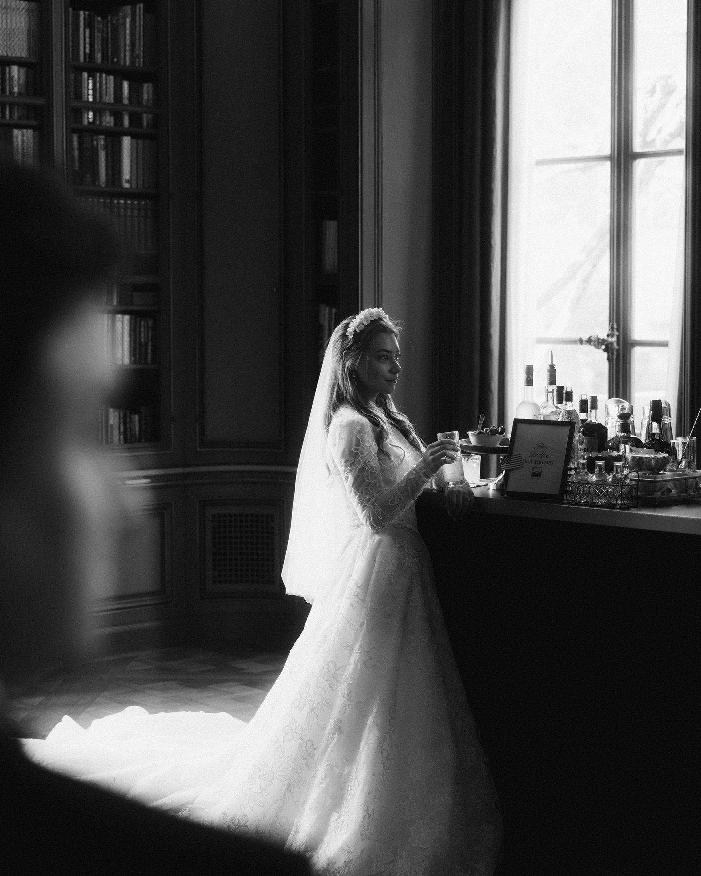 The bride standing at a console against a bright window, her train behind her