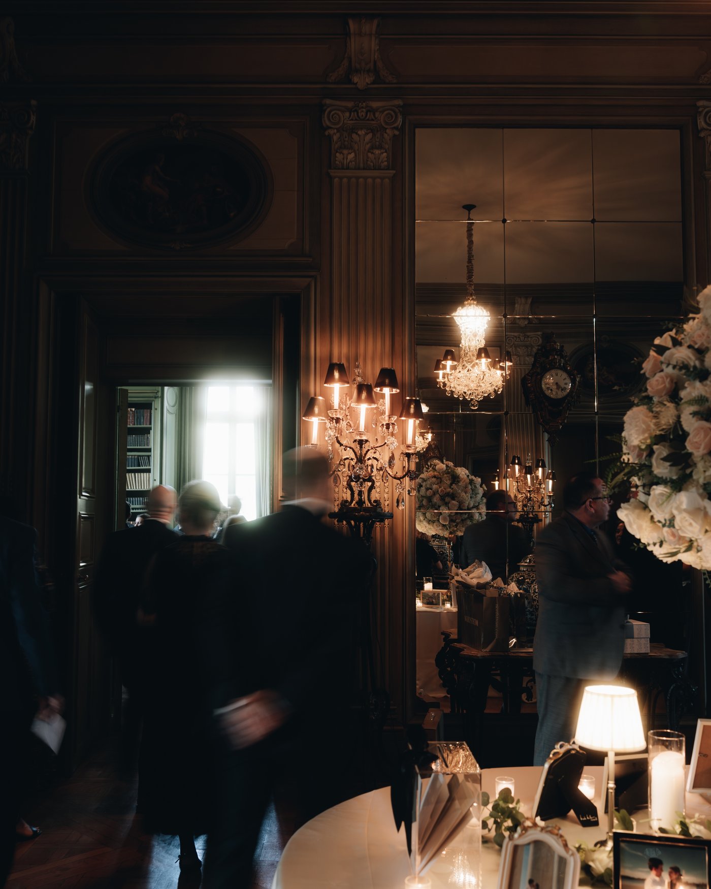 Guests in a warm lamplit room among the flower arrangements