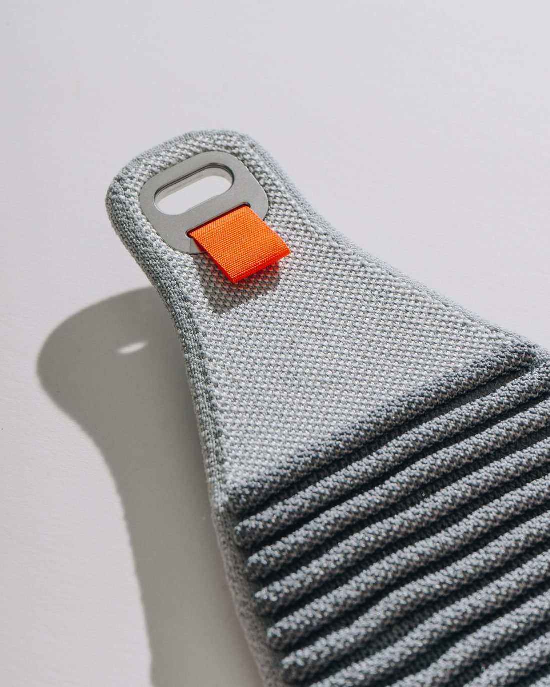 The knitted grey head strap standing on its own on a white surface, throwing a hard shadow