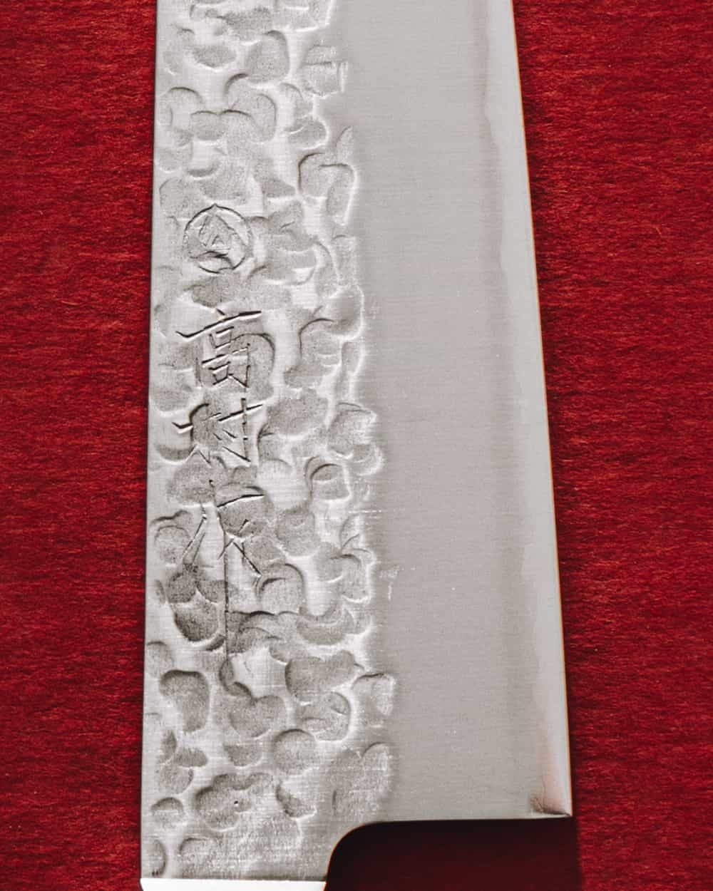Close on the same blade: the dimpled hammer finish and the maker's characters stamped into the steel
