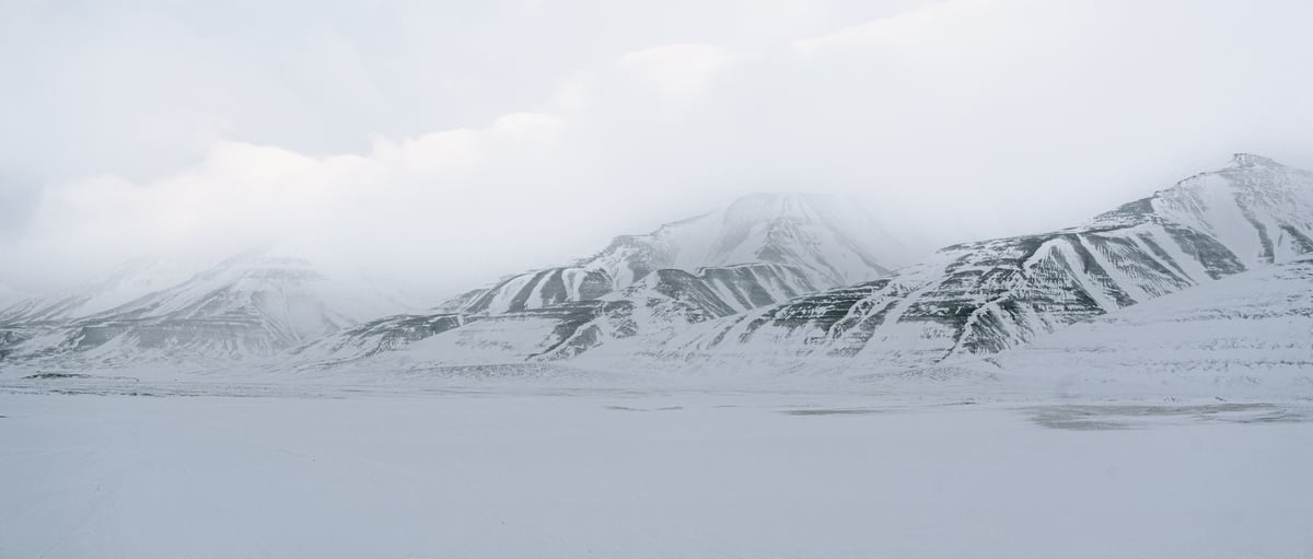 A long range of layered snow mountains under low cloud, seen across a flat frozen plain