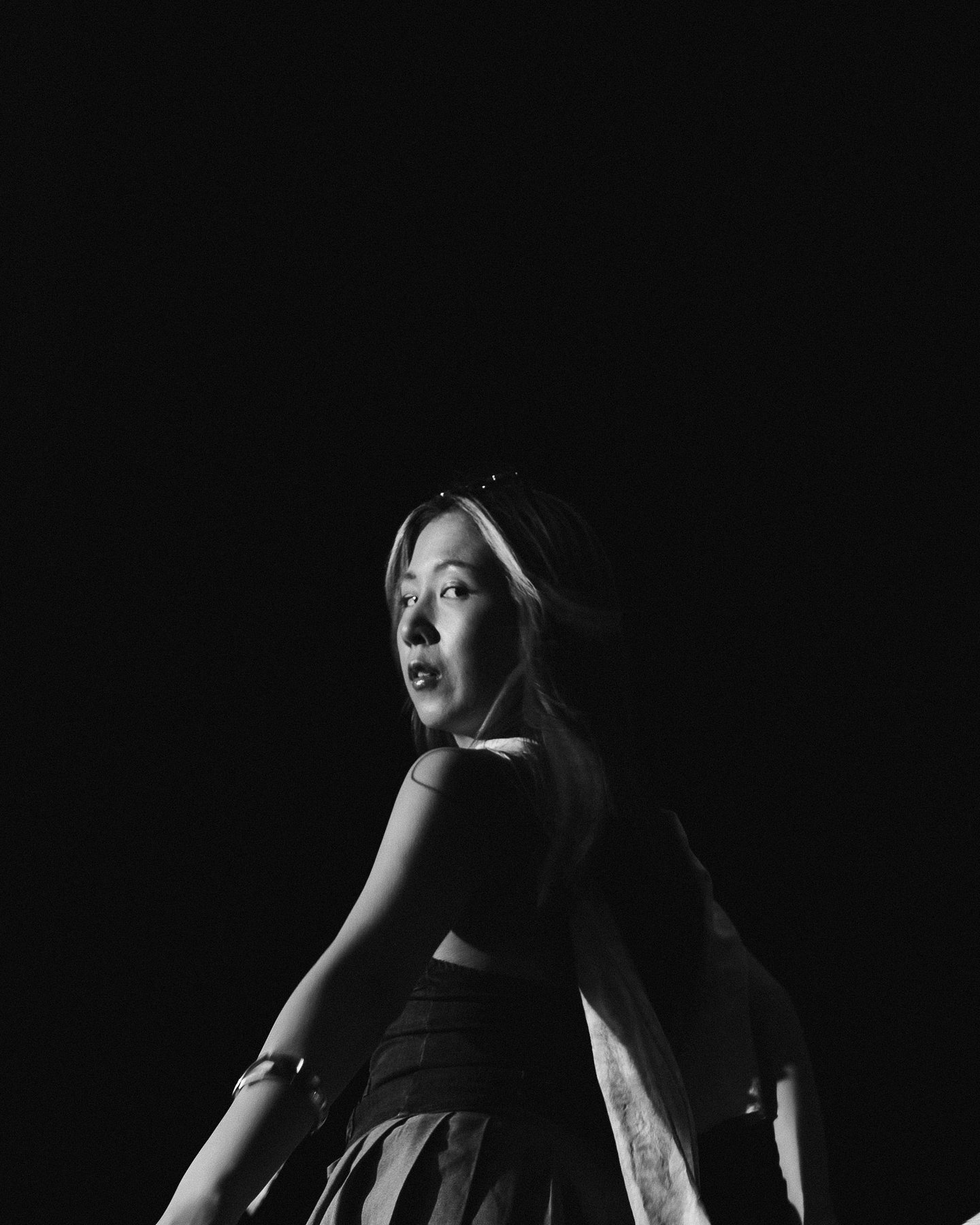Black and white, looking back over a bare shoulder out of the dark