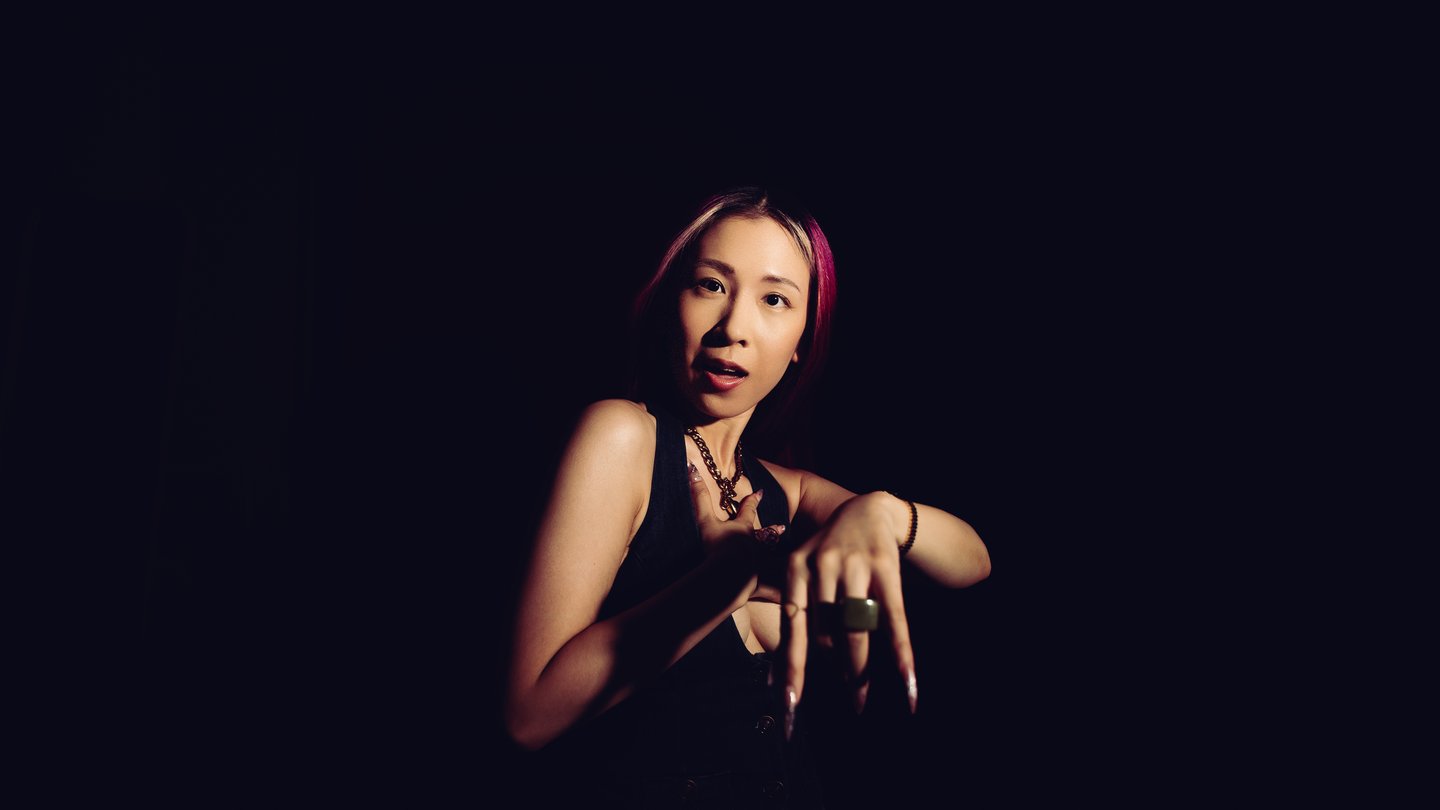 A small figure in the dark, lit from one side, hands raised to the face