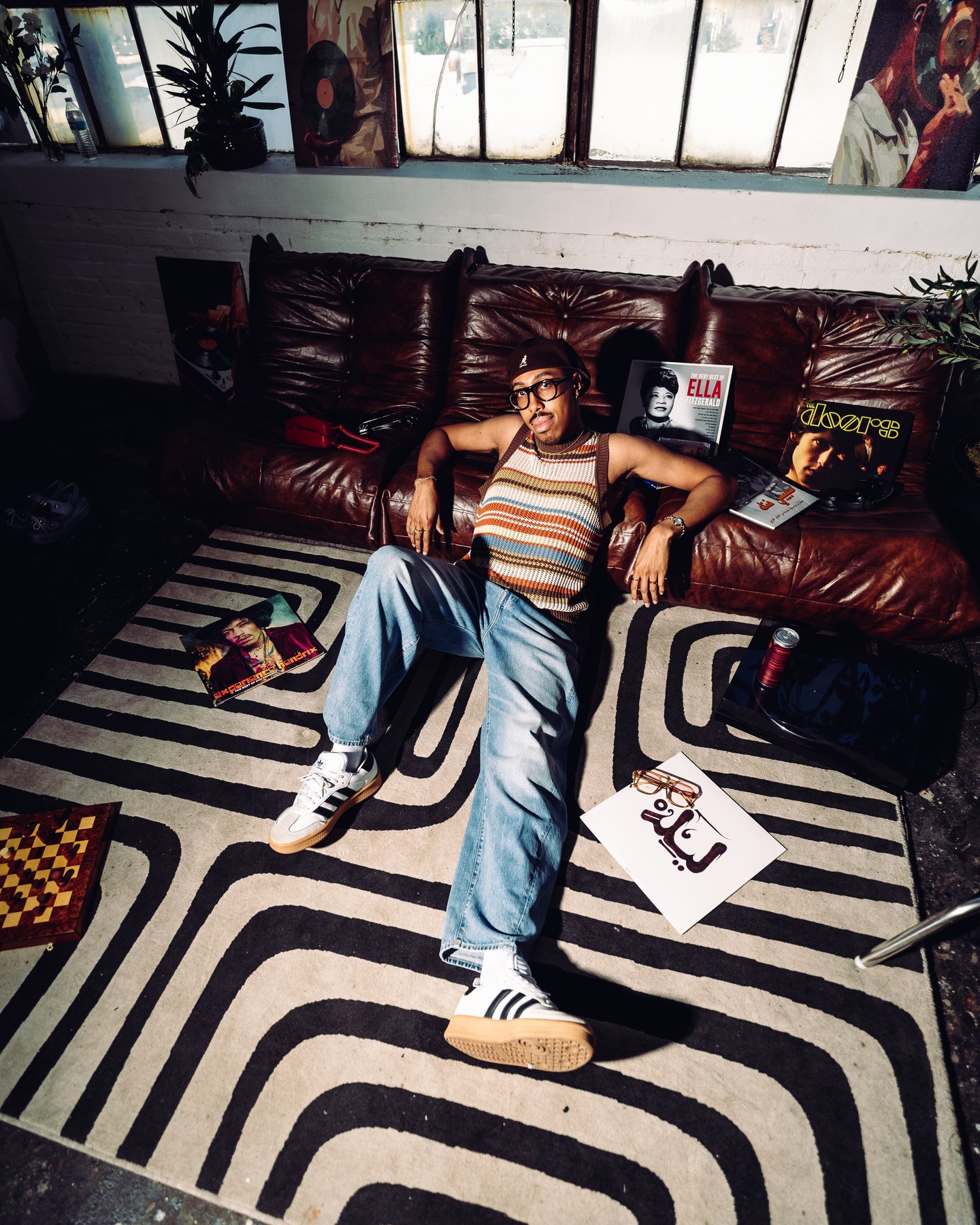 Kyle Starling in a striped tank top and jeans sprawled on the leather sofa, sneakers on the striped rug
