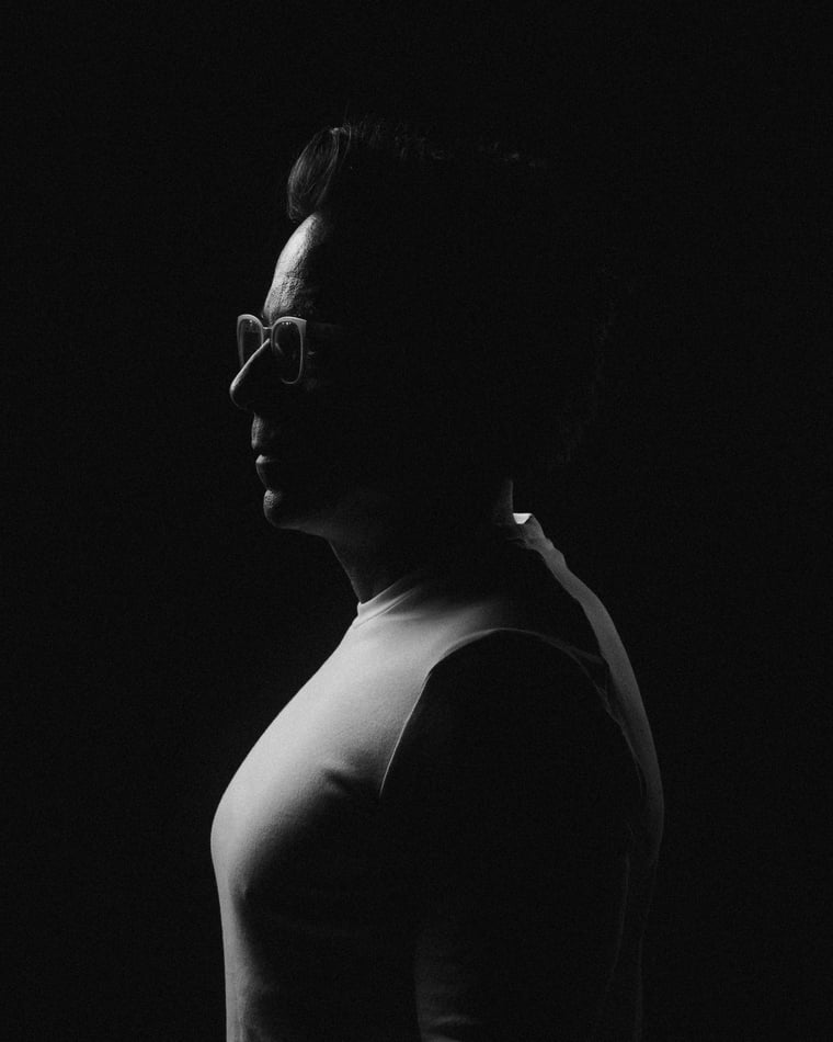 Black and white: a profile in a white vest with the light catching only the edge of a face, a shoulder and an arm