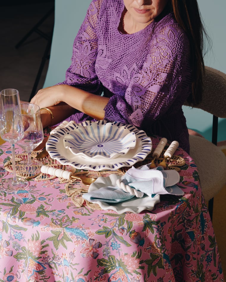 The same table seen wider: a pink floral cloth, gold cutlery, a scalloped shell plate and a napkin dropped loose beside it