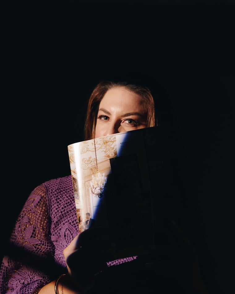 A woman half hidden behind a raised paper fan, lit by a single blade of light in the dark