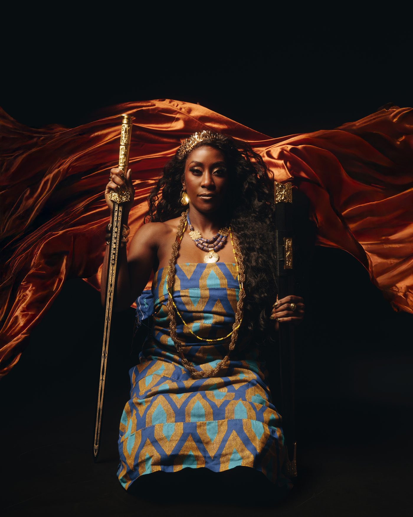 A woman crowned and seated with a long sword held upright in her hand, a red silk cape sweeping out behind her into the black