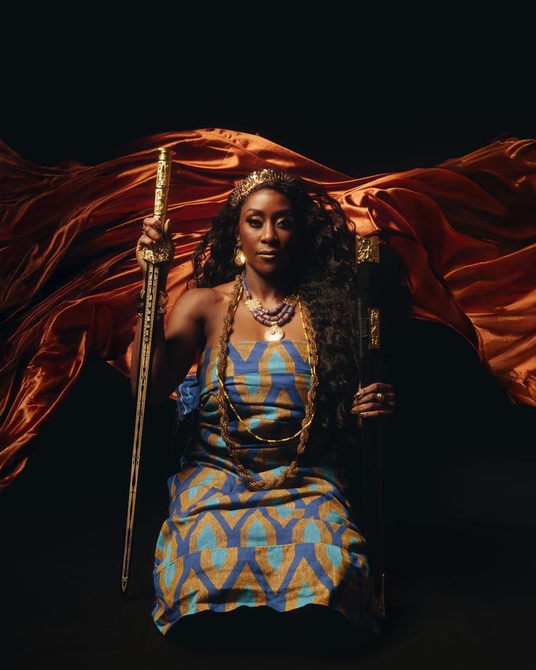 A woman crowned and seated with a long sword held upright in her hand, a red silk cape sweeping out behind her into the black
