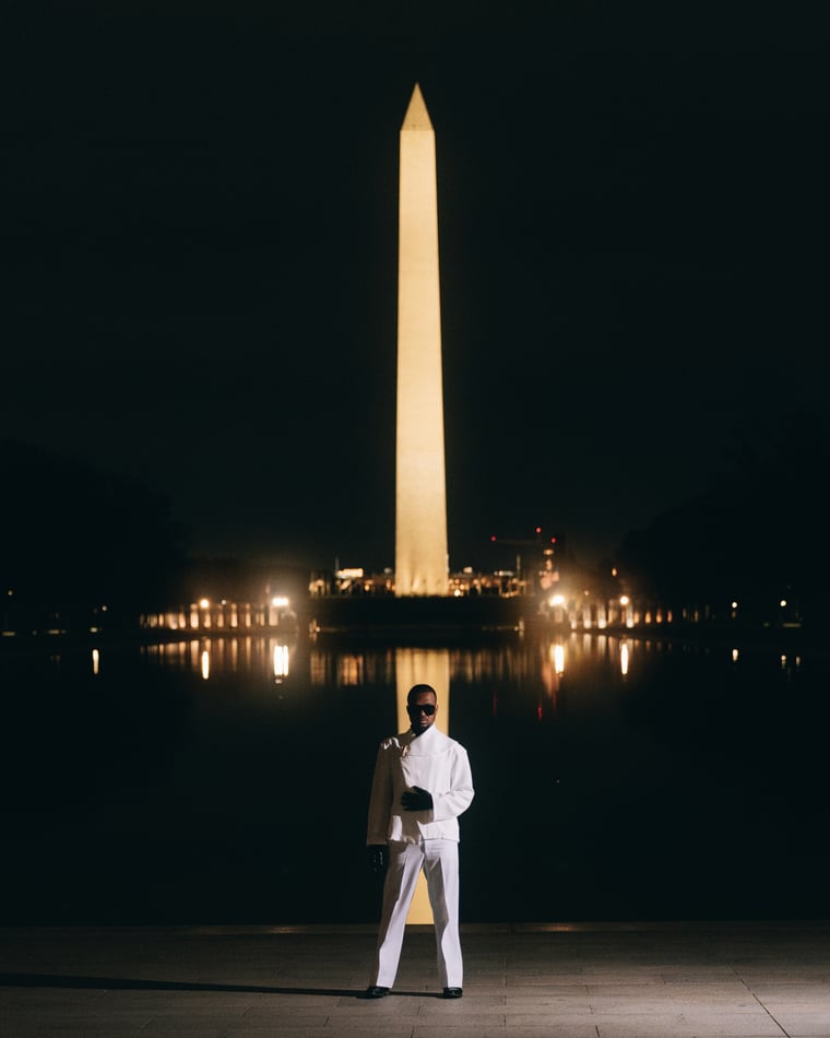 A lone figure dressed in white on the empty plaza at night, the lit obelisk of the Washington Monument rising behind them and repeating in the reflecting pool
