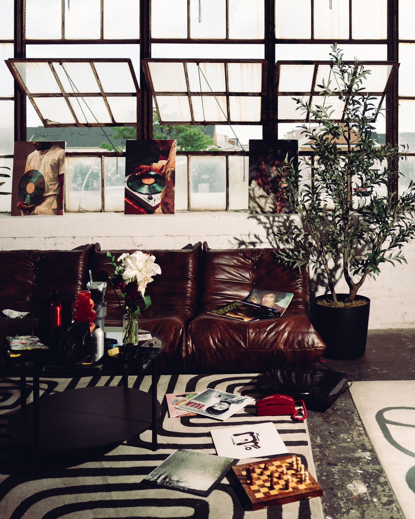 The loft from above: a leather sofa, potted trees, prints and a chessboard on the striped rug