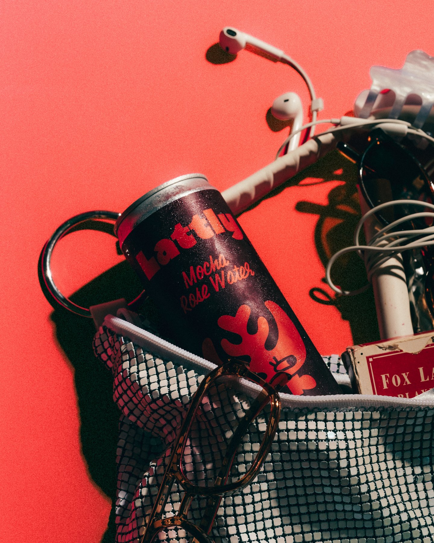 A mesh bag spilling a Lattly can, a keychain and a pack of gum onto red